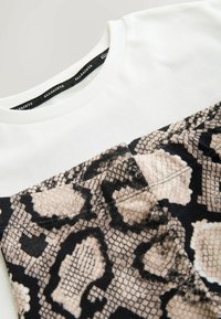 T-shirt blanc à col rond avec un motif de peau de serpent imprimé sur la poitrine et une étiquette noire AllSaints à l'intérieur du col.