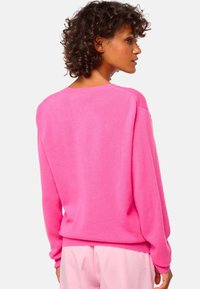 Pull en tricot rose avec un col rond, des épaules tombantes et des poignets côtelés. Le dos présente une texture lisse et une coupe décontractée.