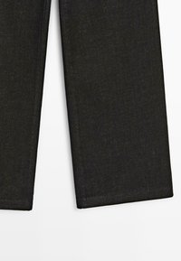 Pantalons en denim noir à coupe droite, avec une texture lisse et des ourlets soigneusement finis. Aucun signe d'usure ou d'ornementation visible.
