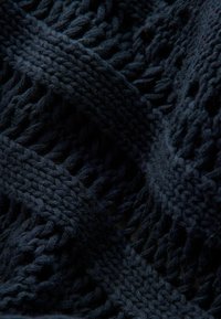 Tamno plavi pletivi materijal s teksturiranim, otvorenim tkanjem s debelim, međusobno povezanim nitima i mekim završetkom.