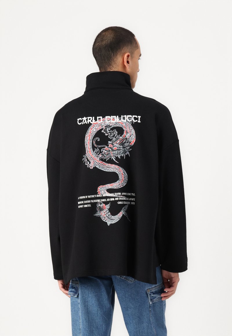 Zwarte oversized sweater met een rode en witte draakafbeelding op de achterkant en branded tekst boven de illustratie.