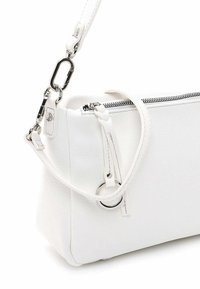 Biała torebka ze skóry o fakturze, z srebrnym zamkiem błyskawicznym, odpinanym paskiem, detalem w postaci pierścienia oraz wytłoczonym logo "Suri Frey" w dolnym rogu.