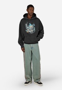 Μαύρη φούτερ με κουκούλα και γραφικό μοτίβο που απεικονίζει μια χειμερινή σκηνή. Συνδυάζεται με ανοιχτό μπλε τζιν παντελόνι με πλευρικές ρίγες και μαύρα αθλητικά παπούτσια.