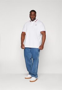 White polo shirt with a red and navy collar, paired with light blue baggy jeans. Complete with white sneakers and a textured finish.