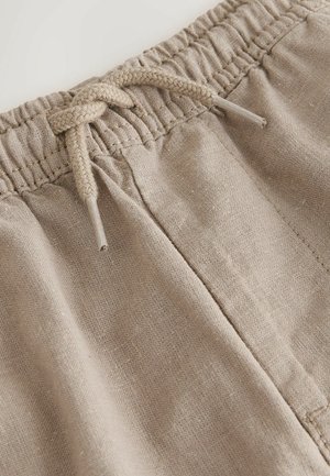 Shorts en lin beige avec une ceinture élastique et un cordon tressé. Le détail de la texture du tissu et des coutures est visible.