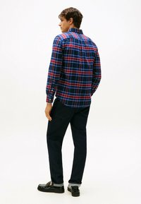 Karierter Flanellhemd in Blau, Rot und Weiß, mit Button-Down-Kragen und langen Ärmeln. Getragen mit dunklen Jeans und schwarzen Schuhen.