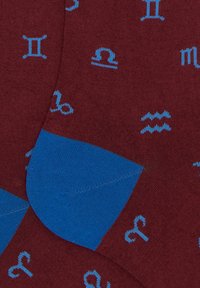 Burgunderfarbene Socken mit hellblauen astrologischen Symbolen, einem strukturierten blauen Bündchen und glattem Stoff überall.