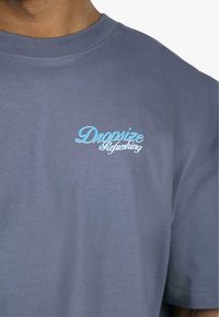 Grå kortærmet t-shirt lavet af bomuld, med et lysblå broderet logo "Dropsize Refreshing" på venstre bryst.
