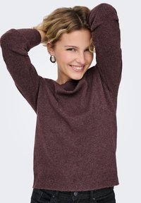 Vinröd tröja med långa ärmar, strukturerat tyg och en rundad halsringning. Bärs med svarta jeans som är löst sittande och korta i längden.