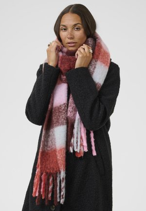 Écharpe en laine avec un motif à carreaux dans des nuances de rouge, rose et blanc, avec des bords effilochés, portée sur un manteau noir.