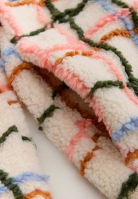 Textured blanket in cream, featuring colorful geometric patterns in pink, green, blue, and brown. Soft, fluffy wool material.