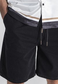 Shorts noirs avec une texture douce, dotés d'une taille élastique et d'un cordon de serrage, associés à une chemise boutonnée blanche et marine élégante.