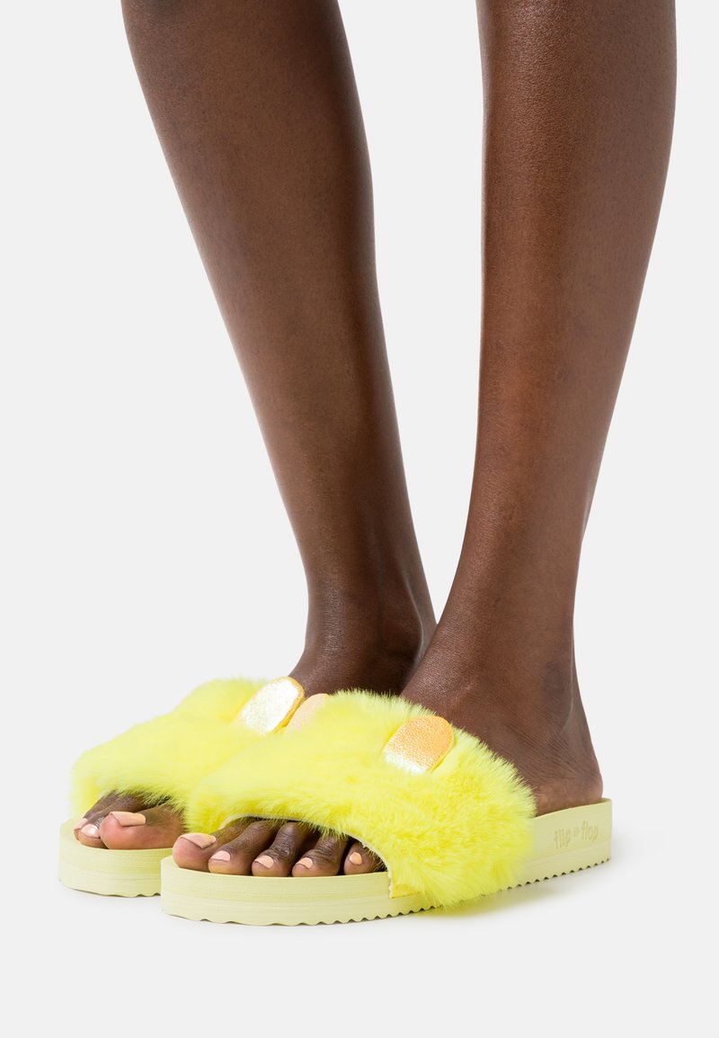 Yellow faux fur slide sandals with shiny gold accents, a textured sole, and open-toe design, showing a soft, fluffy appearance.