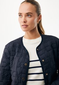 Granatowa pikowana kurtka z geometrycznym wzorem, złotymi zatrzaskami i okrągłym kołnierzem. Nosi się ją na kremowy sweter w granatowe paski.