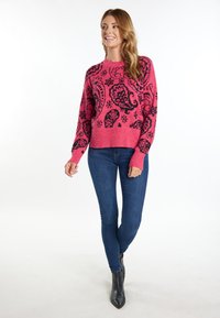 Różowy sweter dziany z czarnym wzorem paisley, z prążkowanymi mankietami i dołem, zestawiony z niebieskimi wąskimi dżinsami i czarnymi botkami za kostkę.