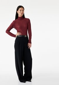 Langsleeve bordeaux turtleneck met zwarte wijde broek. De outfit heeft een zwarte riem met een gouden gespaccent.