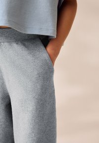 Pantaloni felpa grigi in cotone con una vestibilità rilassata, tasche laterali e una texture morbida, abbinati a un top corto azzurro.