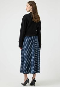 Czarny dziergany sweter w połączeniu z granatową spódnicą midi w groszki. Spódnica ma satynowe wykończenie, a czarne szpilki mają szpiczasty nosek.