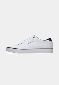 Baskets basses blanches avec détail de talon noir, lacets blancs et logo Tommy Hilfiger sur le côté et la languette, fine bande noire près de la semelle.