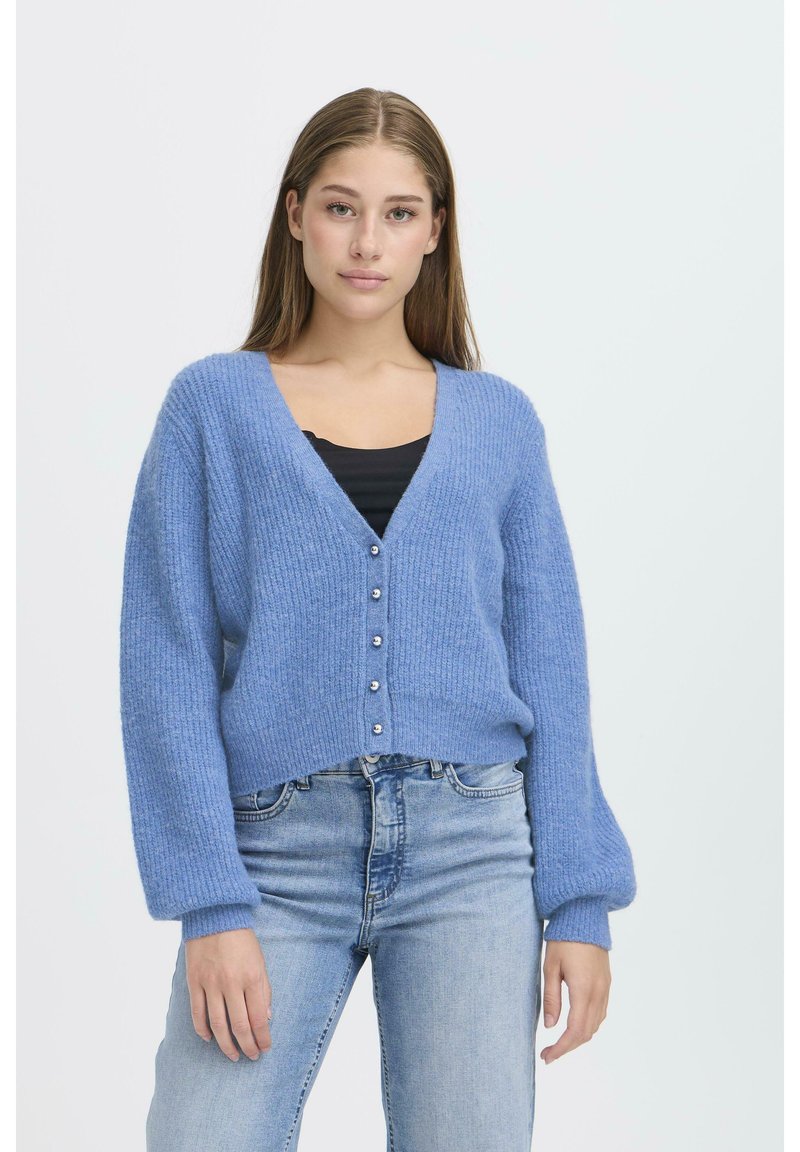 Cardigan lavorato a maglia azzurro chiaro con texture a costine, scollatura a V profonda, cinque bottoni argentati e maniche a sbuffo, abbinato a una maglietta nera e jeans blu.