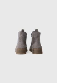 Bottines en daim grises avec un panneau latéral texturé, dotées d'une fermeture éclair à l'arrière et d'une semelle en caoutchouc marron. Design minimaliste, sans embellissements visibles.