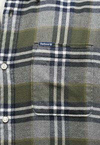 Καρό πουκάμισο σε γκρι, πράσινο και ναυτικό μπλε με τσέπη στο στήθος. Διαθέτει κουμπιά και ετικέτα Barbour. Μαλακό ύφασμα με διαφορετικά μοτίβα.