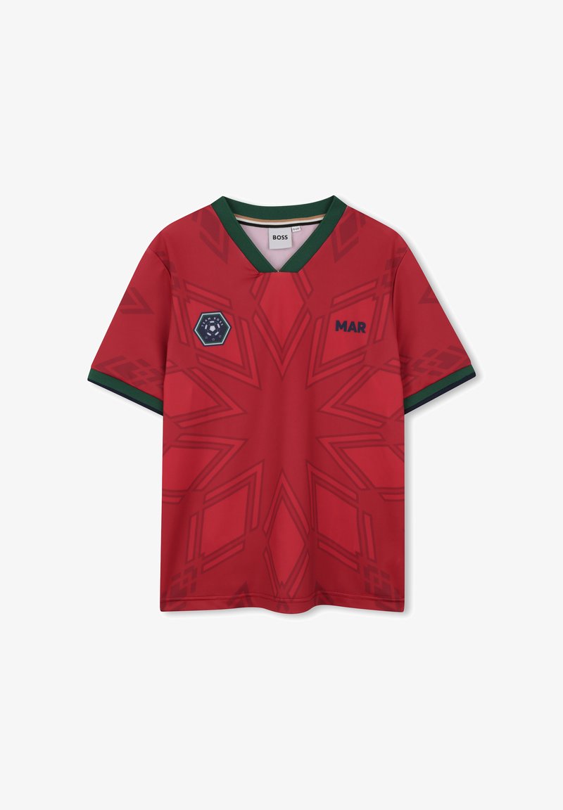 Maglia rossa a maniche corte con scollo a V, caratterizzata da motivi geometrici in tonalità di rosso più scuro, dettagli verdi su collo e maniche, e un emblema esagonale.