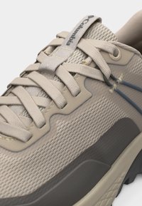 Μπεζ αθλητικό παπούτσι Columbia με πανί από δίχτυ, διασταυρωμένα κορδόνια, ενισχυμένες θηλιές και ορατή υφή γκρι σόλας.