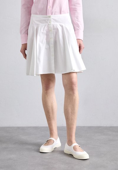 Weißer Knopf-Rock mit weit ausgestellt Design, leichtem Stoff und dezenten Falten. Kombiniert mit weißen Slippern und einem rosa Shirt.