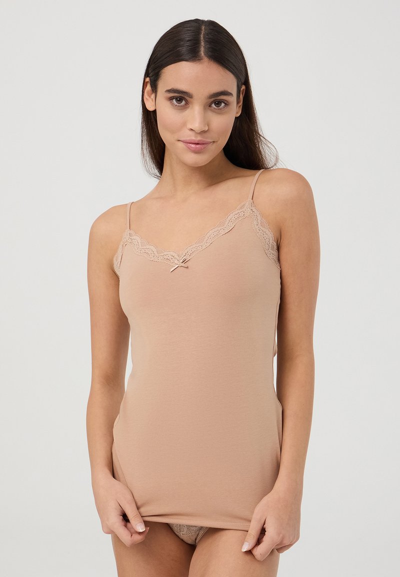 Camisola beige con pizzo lungo l'escote, spalline a farfalla, materiale in cotone morbido e un piccolo nodo decorativo al centro davanti.