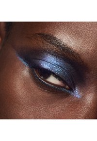 Nahaufnahme eines dunkelhäutigen Auges mit schimmerndem blauen und lila Lidschatten sowie schwarzem Eyeliner, der einen kühnen, dramatischen Makeup-Look kreiert.
