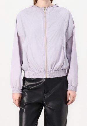 Lichtpaarse capuchonvest met rits, elastische manchetten en tailleband, gedragen met zwarte leren broek.