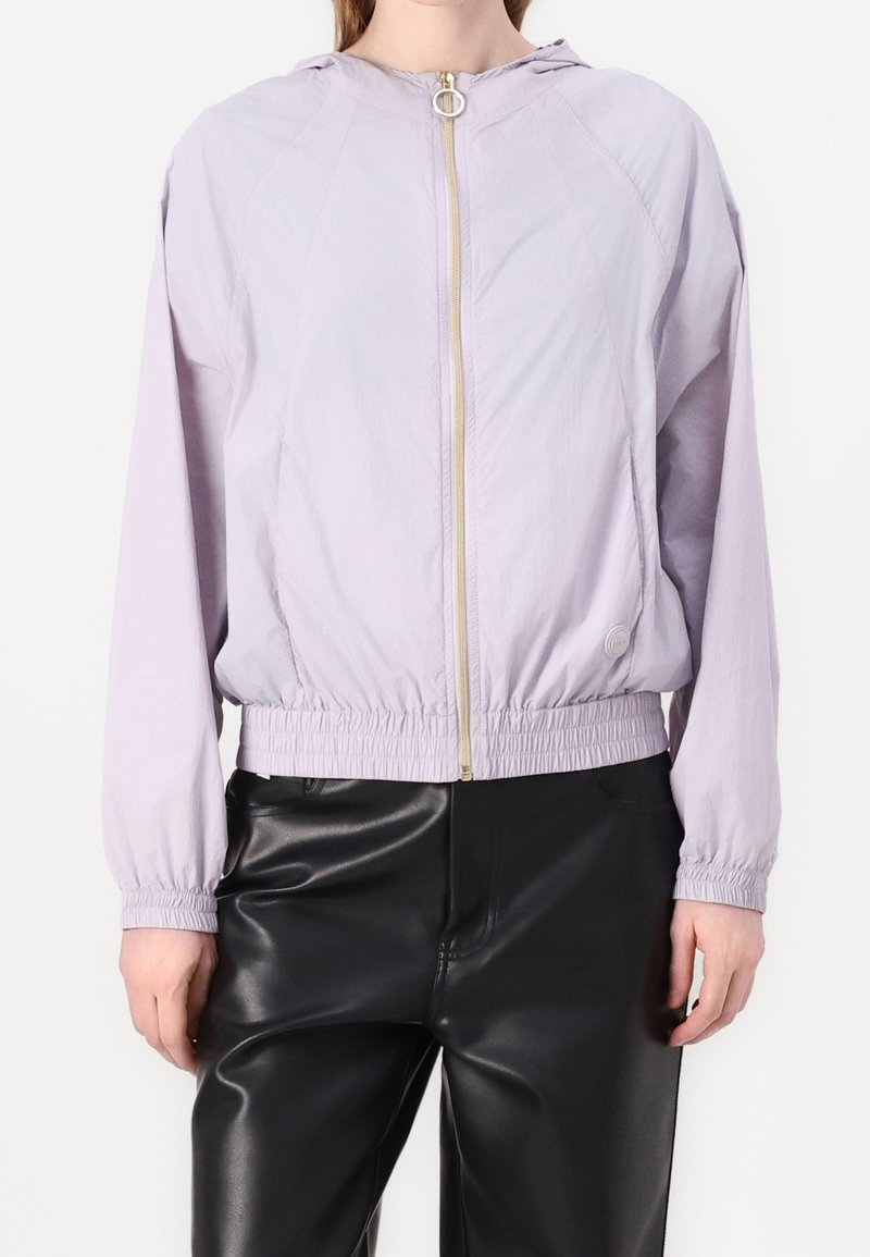 Lyse lilla hættejakke med lynlås, elastiske manchetter og talje, båret sammen med sorte læderbukser.