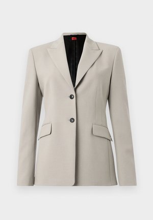 Lys grå blazer med skødder, to knaplukninger og to frontlommer. Glat stof med skræddersyet pasform og sort indvendig foering.