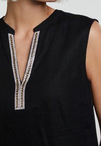 Zwarte linnen top met een V-hals en decoratieve kralen en kettingaccenten langs de halslijn. Mouwloos ontwerp met een ontspannen pasvorm.