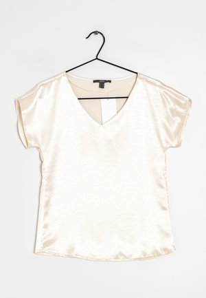 Top in satin beige chiaro con scollatura a V e maniche corte, caratterizzato da una superficie liscia e un orlo curvo. Appeso a un gancio nero.