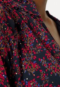 Tessuto nero con stampa floreale caratterizzato da foglie rosse e blu, intervallate da accenti dorati. Texture liscia con un design drappeggiato.