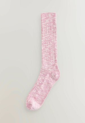Knähöga rosa och vita melerade stickade strumpor med ribbat mönster, liggande platt på en neutral bakgrund.