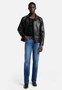 Svart läderjacka, åtsittande svart linne, ljusblå raka jeans och svarta stövlar. Modellen står mot en enkel vit bakgrund.