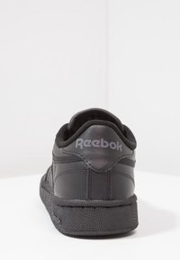 Baskets noires Reebok avec dessus en cuir lisse, col rembourré, semelle en caoutchouc texturée et logo de la marque à l'arrière. Design minimaliste.
