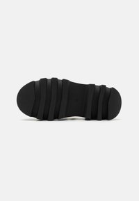 Black rubber shoe sole with a ridged pattern, featuring prominent grooves and a rounded toe, designed for traction and flexibility.
