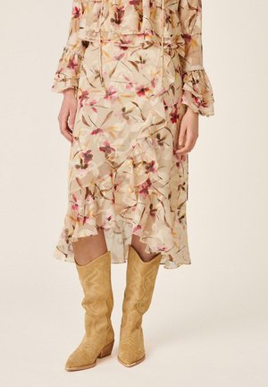 Vestido midi floral beige claro con volantes combinado con botas vaqueras de ante marrón con patrones bordados.