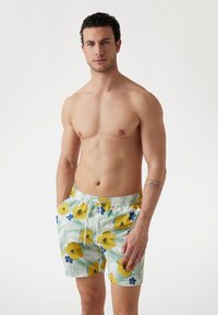 Pantaloni de baie cu imprimeu floral, având un fundal verde deschis, hibiscus galben și flori albastre, cu talie elastică și șnur.