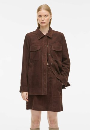 Braune Wildlederjacke mit Kragen, zwei Brusttaschen und Knopfverschluss, kombiniert mit einem passenden Rock, glatte Textur, minimalistisches Design.