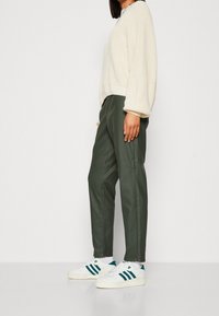 Pull en maille crème avec manches ballon, associé à un pantalon fuselé vert foncé et des baskets blanches avec des rayures vert foncé.