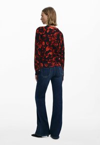 Piros virágmintás, hosszú ujjú blúz fekete háttérrel, sötétkék, bő szabású farmernadrággal párosítva. Az öltözék testhez simuló sziluettet és puha textúrát mutat.