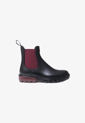 Black Chelsea rain boot with thick tread sole and dark red elastic side panel and heel pull tab.