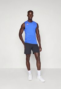 Sinine varrukateta sportlik särk oranži aktsendilogoga, mille juurde on kombineeritud mustad lühikesed püksid oranžide küljetega, kantud valgete tossudega.