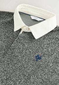 Grå tekstureret polo shirt med hvid krave og blåt logo. Har et vævet herringbone mønster og knaplukning.