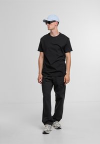 Zwarte katoenen t-shirt, losse pasvorm, gecombineerd met donkere jeans. Lichtblauw petje en donkere zonnebril. Sneakers hebben een grijs en wit ontwerp.
